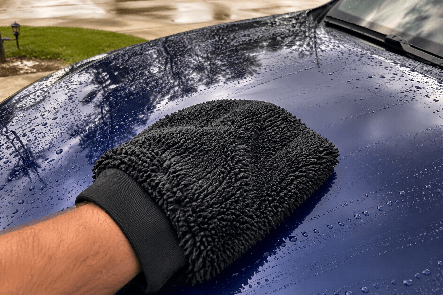 Hand in a black microfiber wash mitt running across a freshly washed dark blue car panel